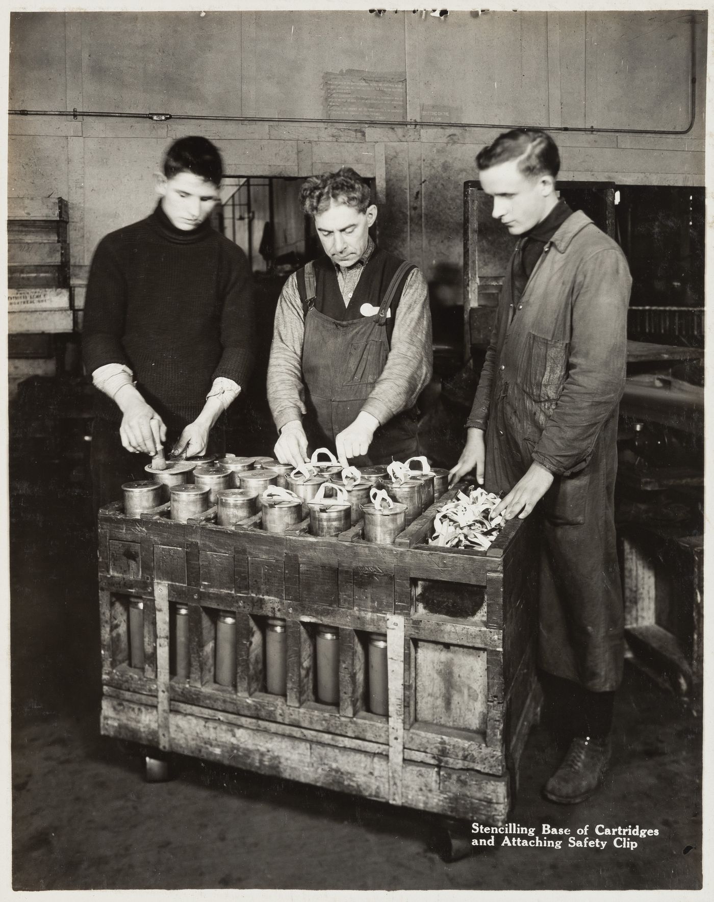 Interior view of workers stencilling base of cartridges and attaching safety clip at the Energite Explosives Plant No. 3, the Shell Loading Plant, Renfrew, Ontario, Canada