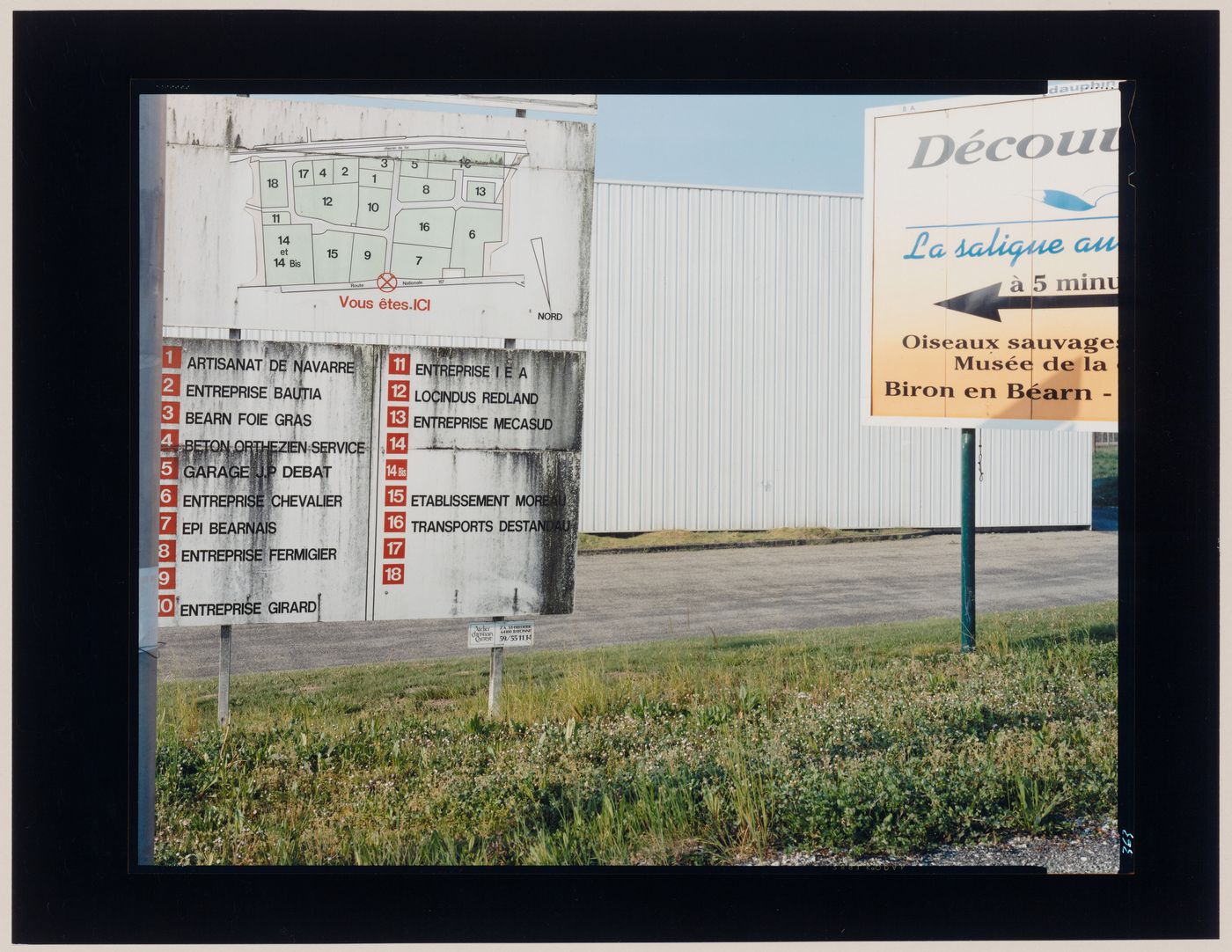 View of signs, a wall covered in metal siding and a driveway, Orthez, France (from the series "In between cities")