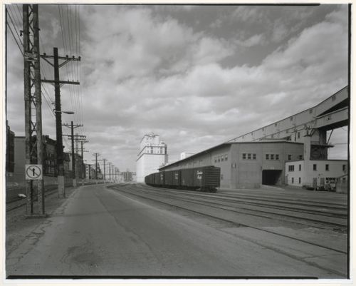 View of Shed No. 11 surmounted by a conveyor gallery with railway cars on the right and Grain Elevator No. 2 (now demolished) in the background, rue de la Commune, Port of Montréal, Québec