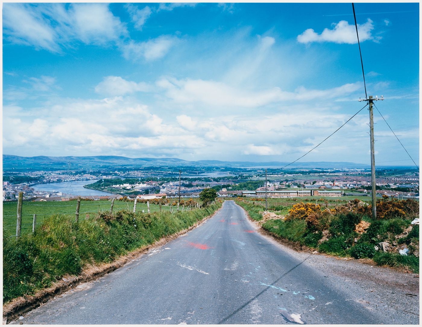 Asphalt road through pastures looking toward city on a river, Derry (Londonderry), Northern Ireland