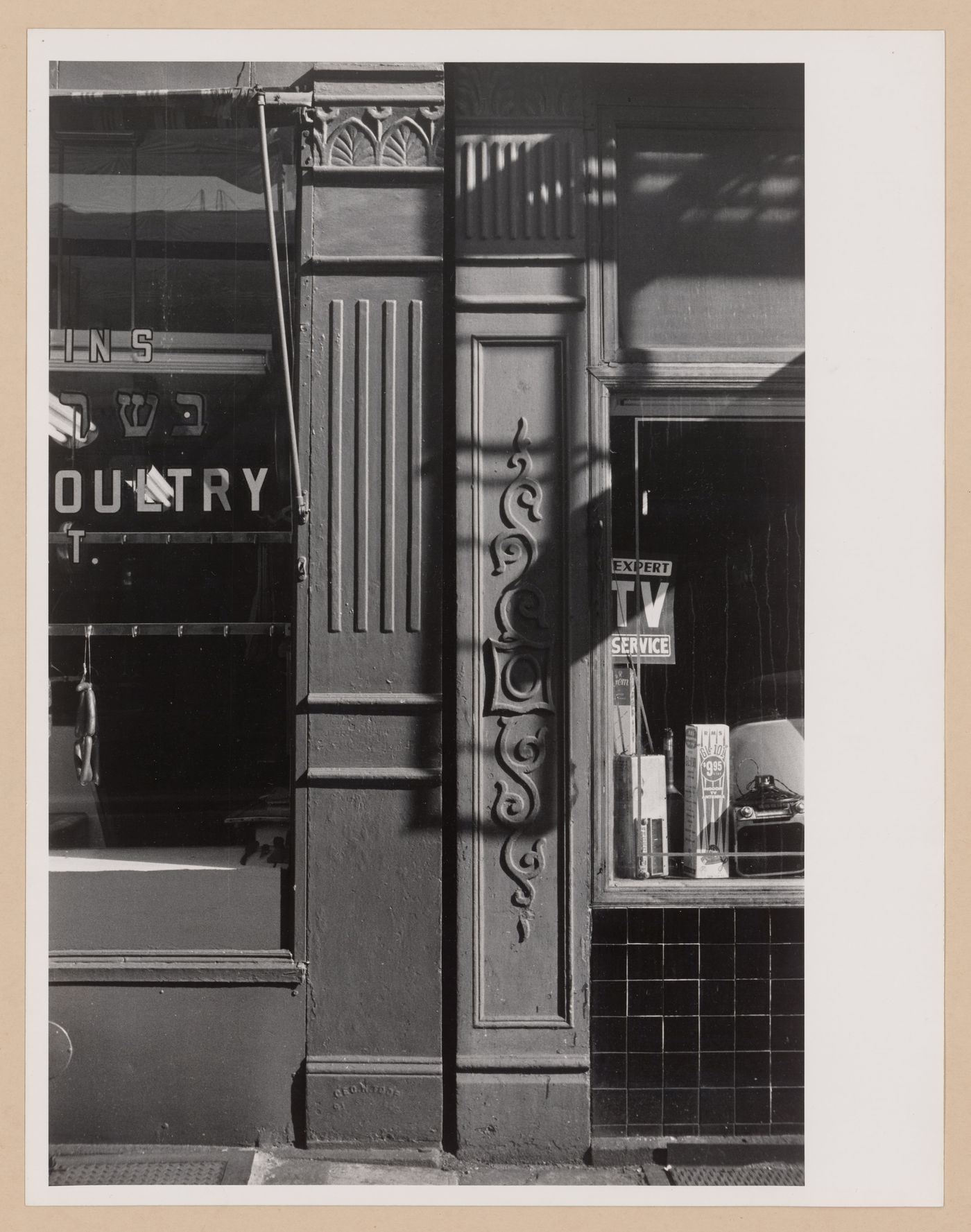 Partial view of two shop façades showing windows, two ornamented columns and the shadow of a fire escape, New York City, New York
