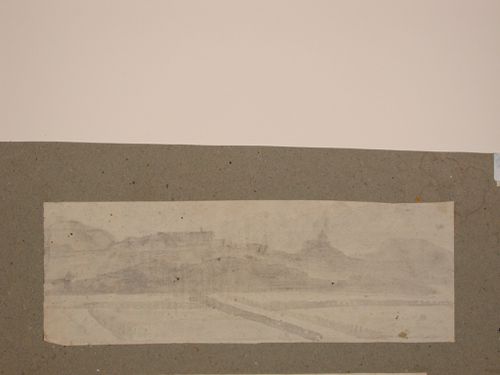 View of a field, with mountains and buildings in the background