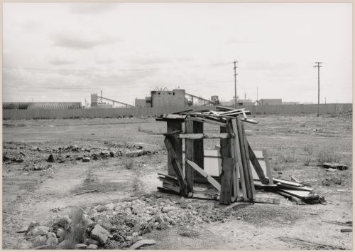 Field Work in Montreal: View of a shack-like structure of wood and corrugated fibreglass, a vacant lot and utility poles showing a metal fence and a processing plant in the background, Montréal, Québec