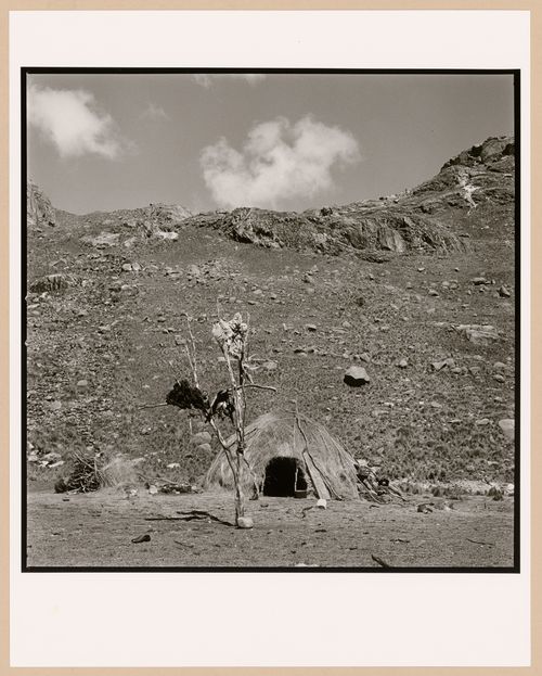View of hut in mountains, two figures sitting next to it, Peru