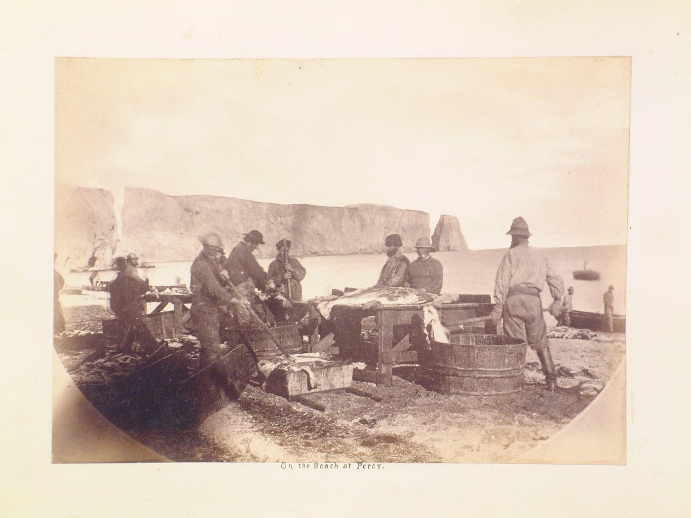 View of men preparing fish on the beach with Percé Rock in the background, Percé, Québec
