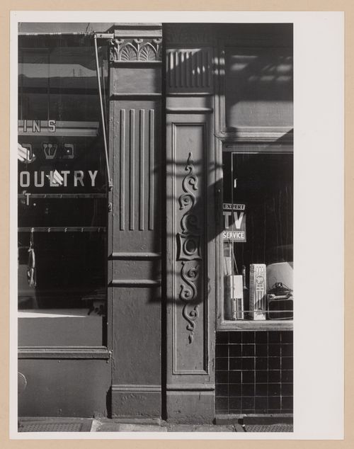 Partial view of two shop façades showing windows, two ornamented columns and the shadow of a fire escape, New York City, New York