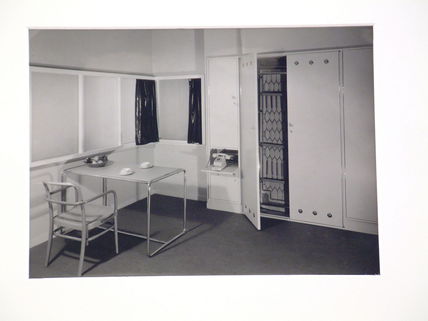 Interior with tubular frame [?] table, plastic curtains, and folding bed in built in cupboard