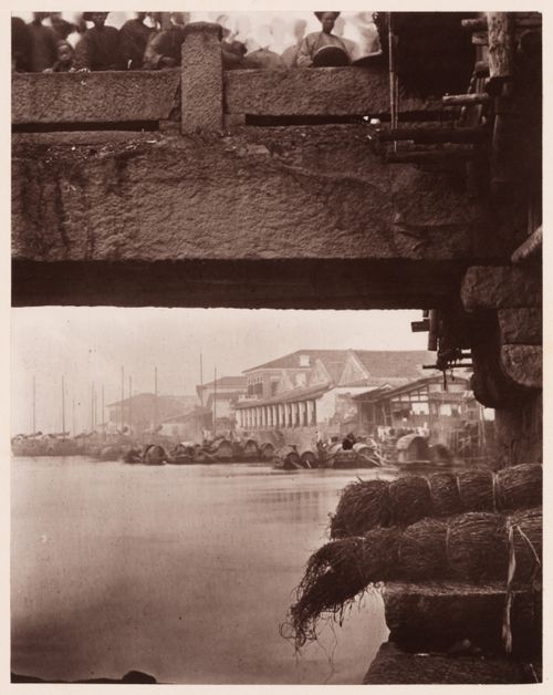 View of the bank of the Min River, with sampans and commercial buildings on the right and the Upper Bridge above, Foochow (now Fuzhou), China