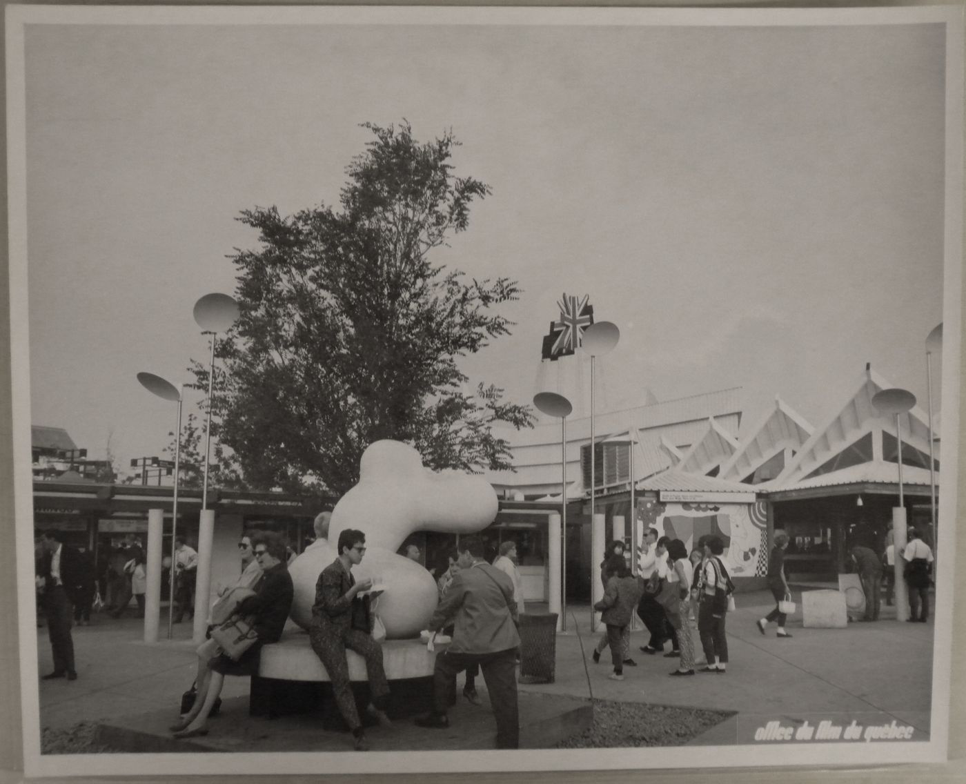 View of a bench topped by a sculpture at the Expo-Services A with the Great Britain Pavilion in background, Expo 67, Montréal, Québec