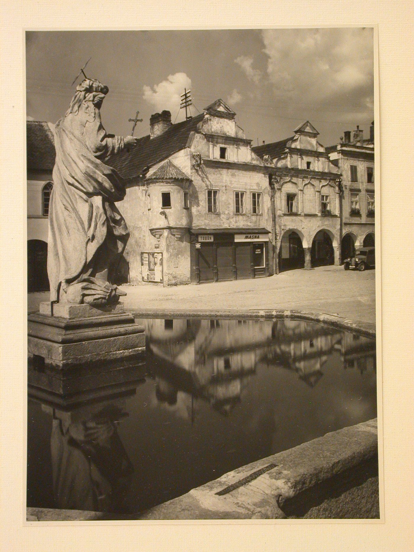 Partial view of a fountain with a statue in the Námestí Míru [Town Square] with buildings in the background, Telc, Czechoslovakia (now Czech Republic)