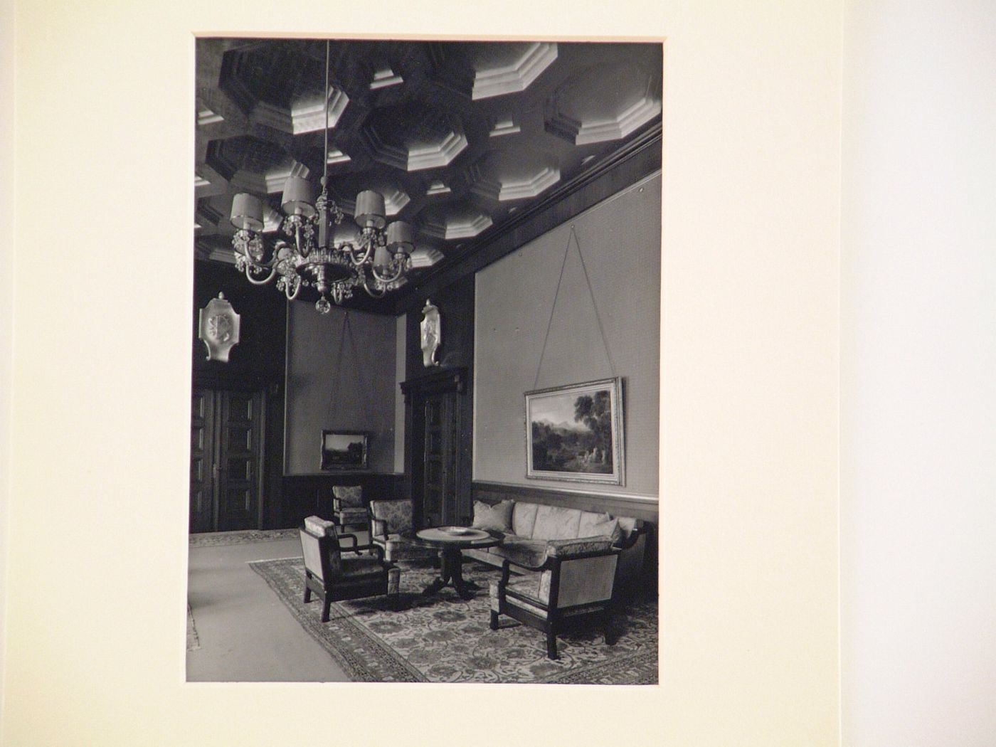 Interior photograph of a large room with coffered ceiling, chandelier, and oil paintings on walls
