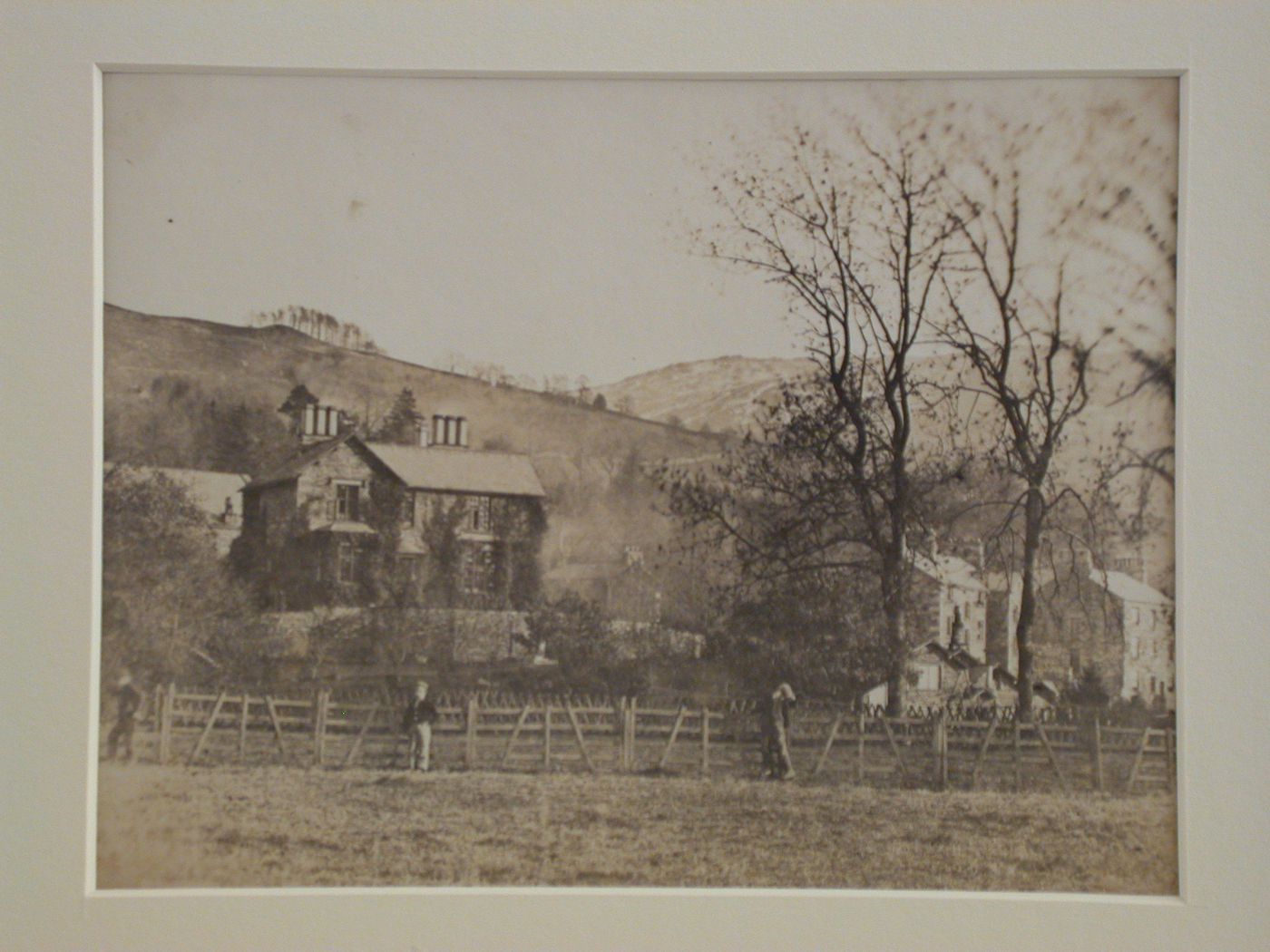 View of three houses on a hillside with a wooden fence and three figures in the foreground, England
