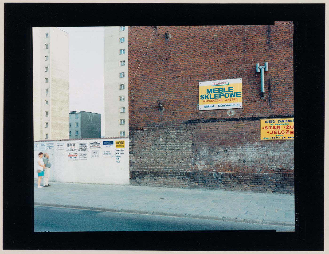 View of walls bearing advertising signs and signs offering medical services showing apartment houses in the background, Malbork, Poland (from the series "In between cities")