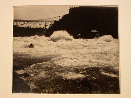 Niagara Falls: Rapids at shore line, trestle bridge with cables in background