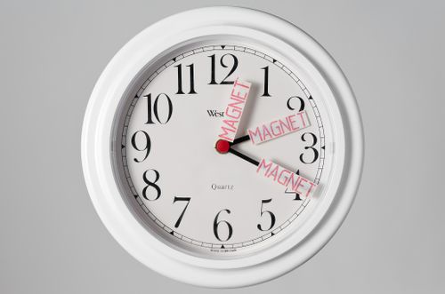 Quartz clock with slips of paper stamped "Magnet" attached to hands