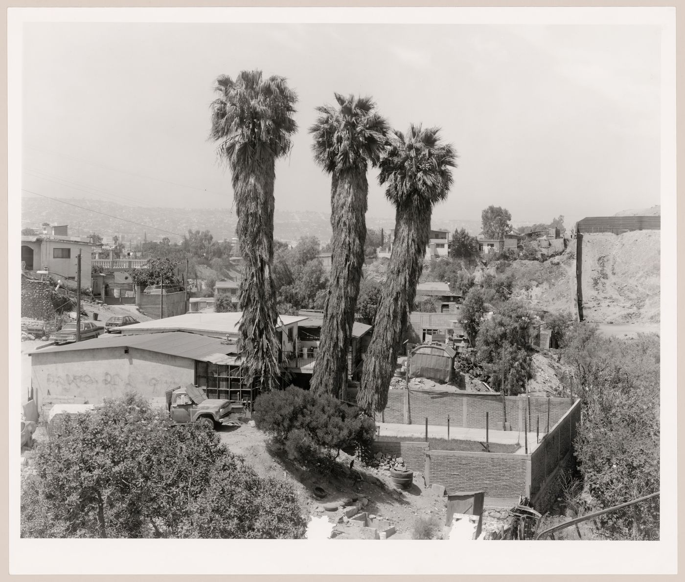 View of Colonia Libertad with trees and houses in the foreground and showing a partial view of the United States-Mexico border fence in the centre right, San Diego County, California, United States, and Colonia Libertad, Tijuana, Baja California, Mexico