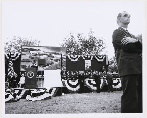 View of the dedication ceremony of the John F. Kennedy Educational, Civic and Cultural Center showing a partial view of the platform with people and a photograph of the model of the building, Mineola, New York
