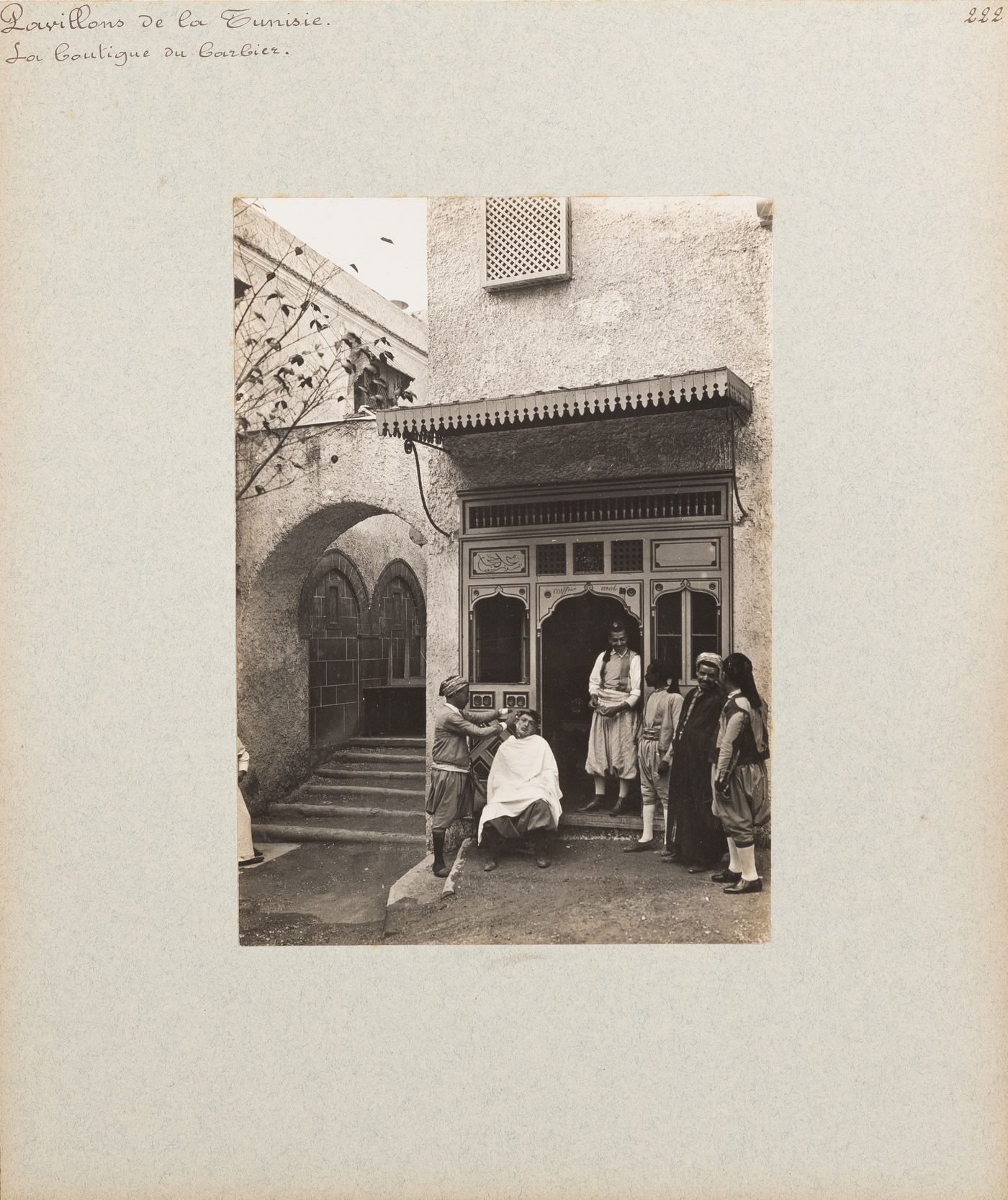 View of people, including barber and client, at entrance to barber shop, Tunisian section, Exposition universelle, 1900, Paris, France