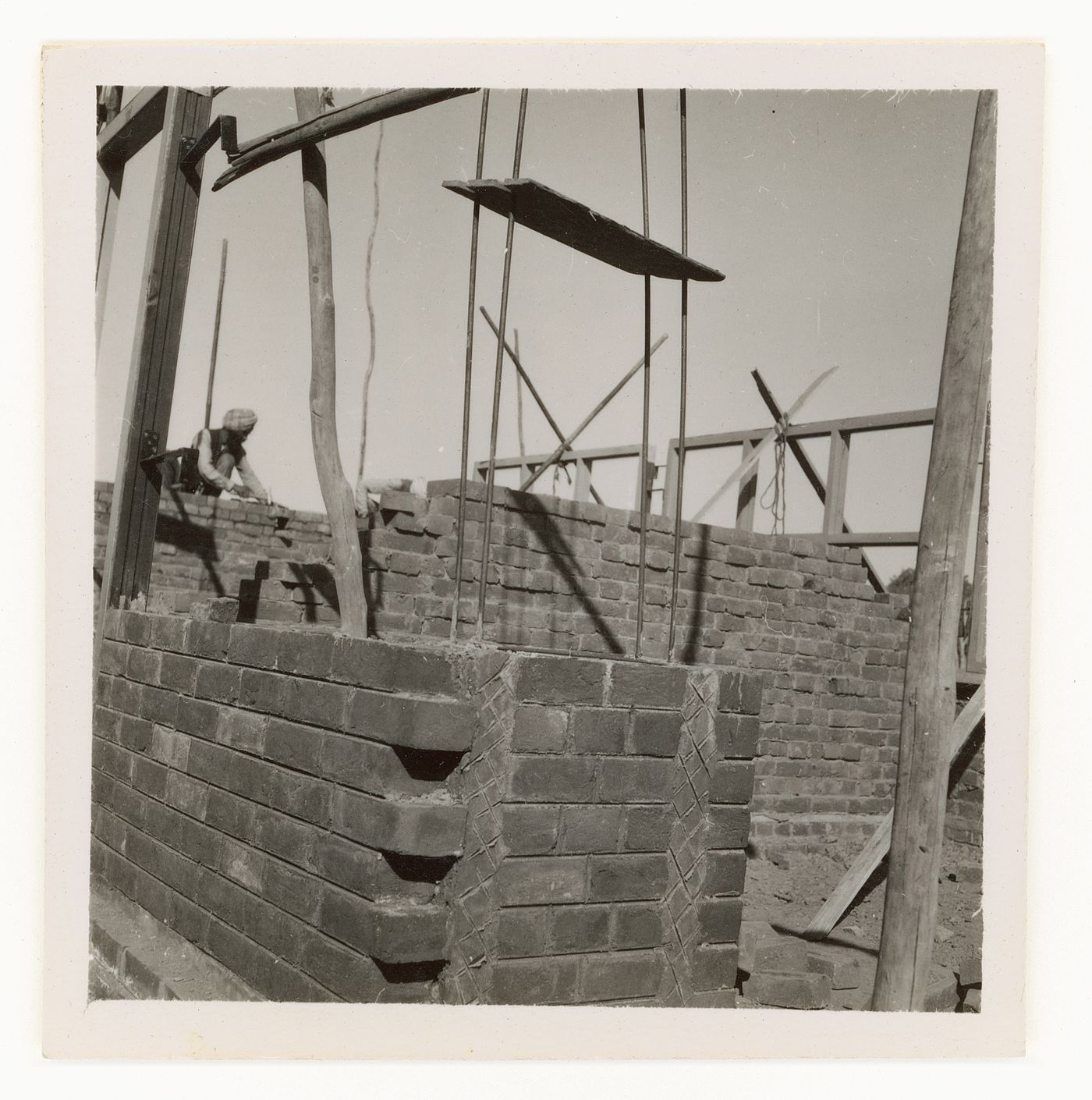 View of brick building under construction, with wooden scaffolding and brick layers in background, Chandigarh, India