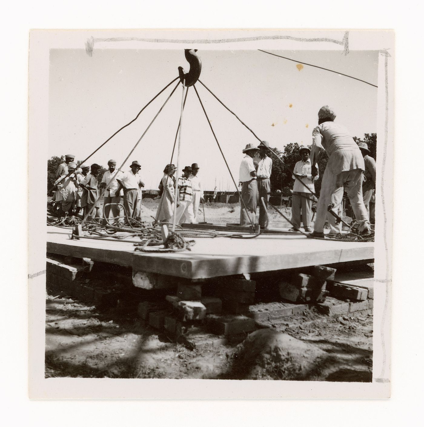 View of people gathering around concrete slab suspended by crane on construction site, Chandigarh, India