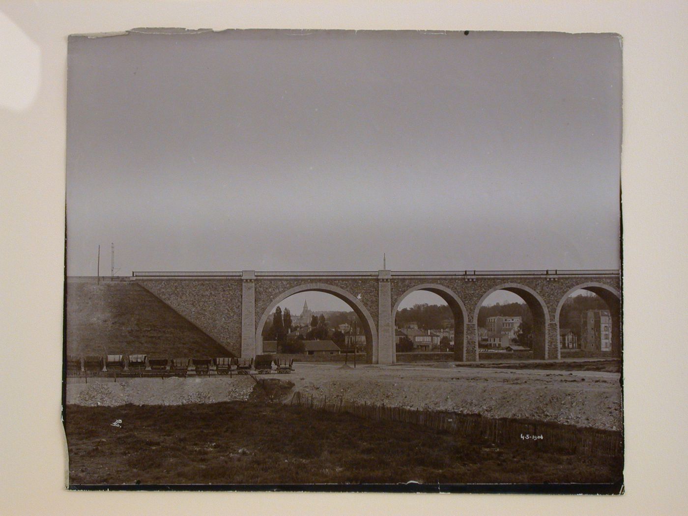 Partial view of a viaduct showing a town in the distance and railroad cars on the left, France ?