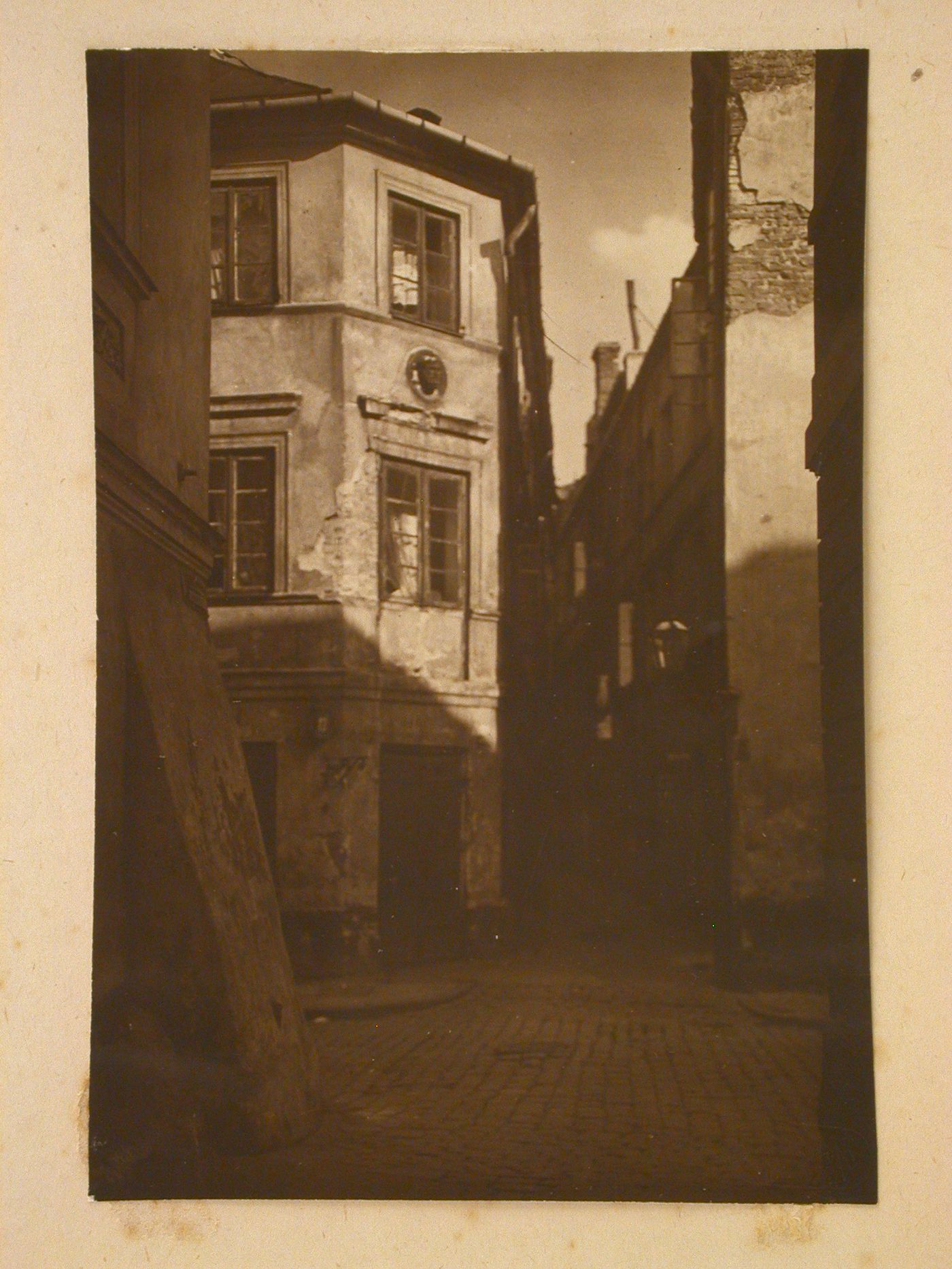 Ground level view of intersection of two small unidentified cobble-stone streets lined with three-storey buildings in disrepair, in the Old Town district, Stare-Miasto, Warsaw, Poland