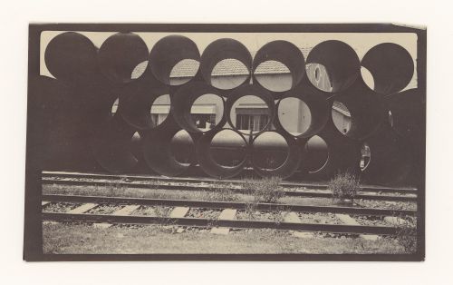 View of riveted pipes stacked next to train tracks, unknown location