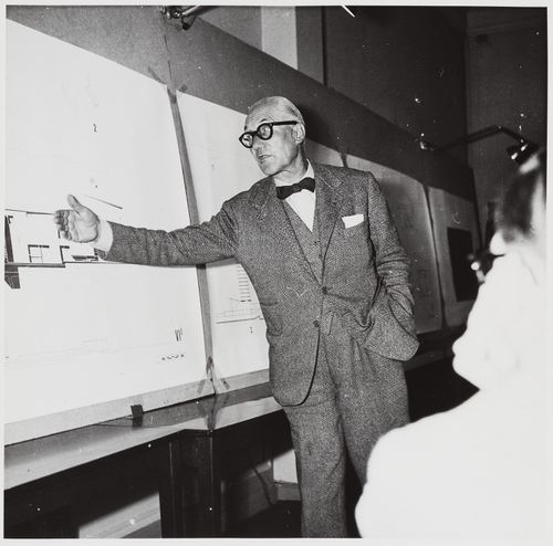 Portrait of Le Corbusier standing in front of presentation drawings for an unidentified project, France [?]