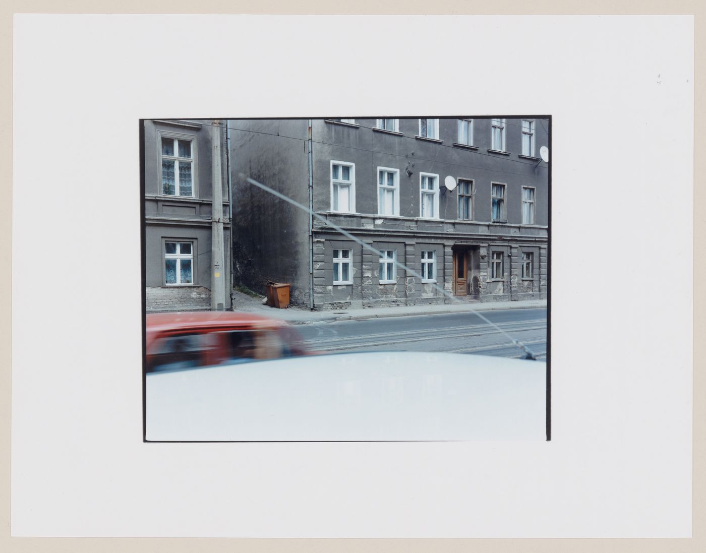 View of buildings and a street showing an automobile and the roof of an automobile in the foreground, Frombork, Poland (from the series "In between cities")