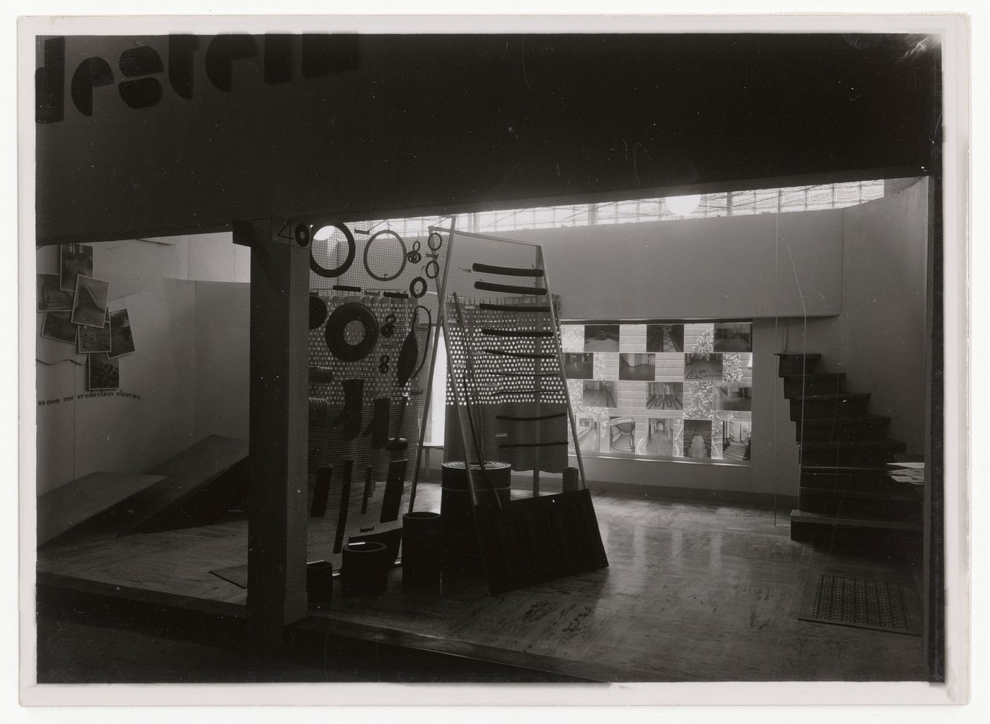 Interior installation view of an exhibition, showing photos mounted on window, and overlapped on wall, and freestanding sculptural elements, Netherlands
