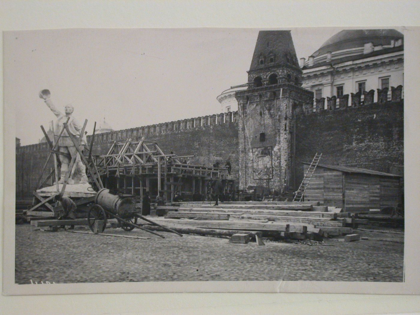 View of the second wooden Lenin Mausoleum under construction with a monument and wooden beams in the foreground, Red Square, Moscow