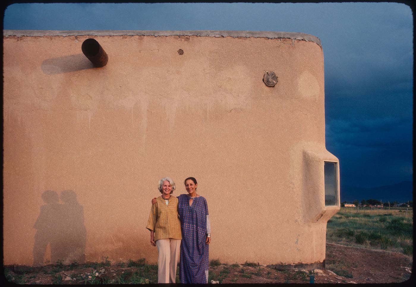 Anne Alpert and Luchita Mullican in front of an adobe building, Taos, New Mexico