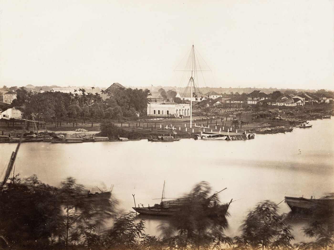View of the flagtower and junks from across the Saigon River [?] with a building under construction in the background, Saigon (now Ho Chi Minh City), Cochin China (now in Vietnam)