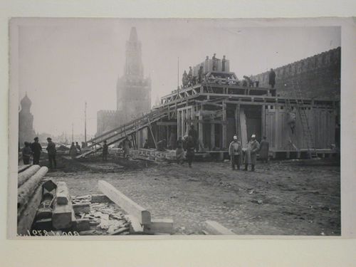 View of the lateral façade of the second wooden Lenin Mausoleum under construction showing wooden beams in the foreground and the Saint Basil Cathedral and the Spasskaia Tower in the background, Red Square, Moscow