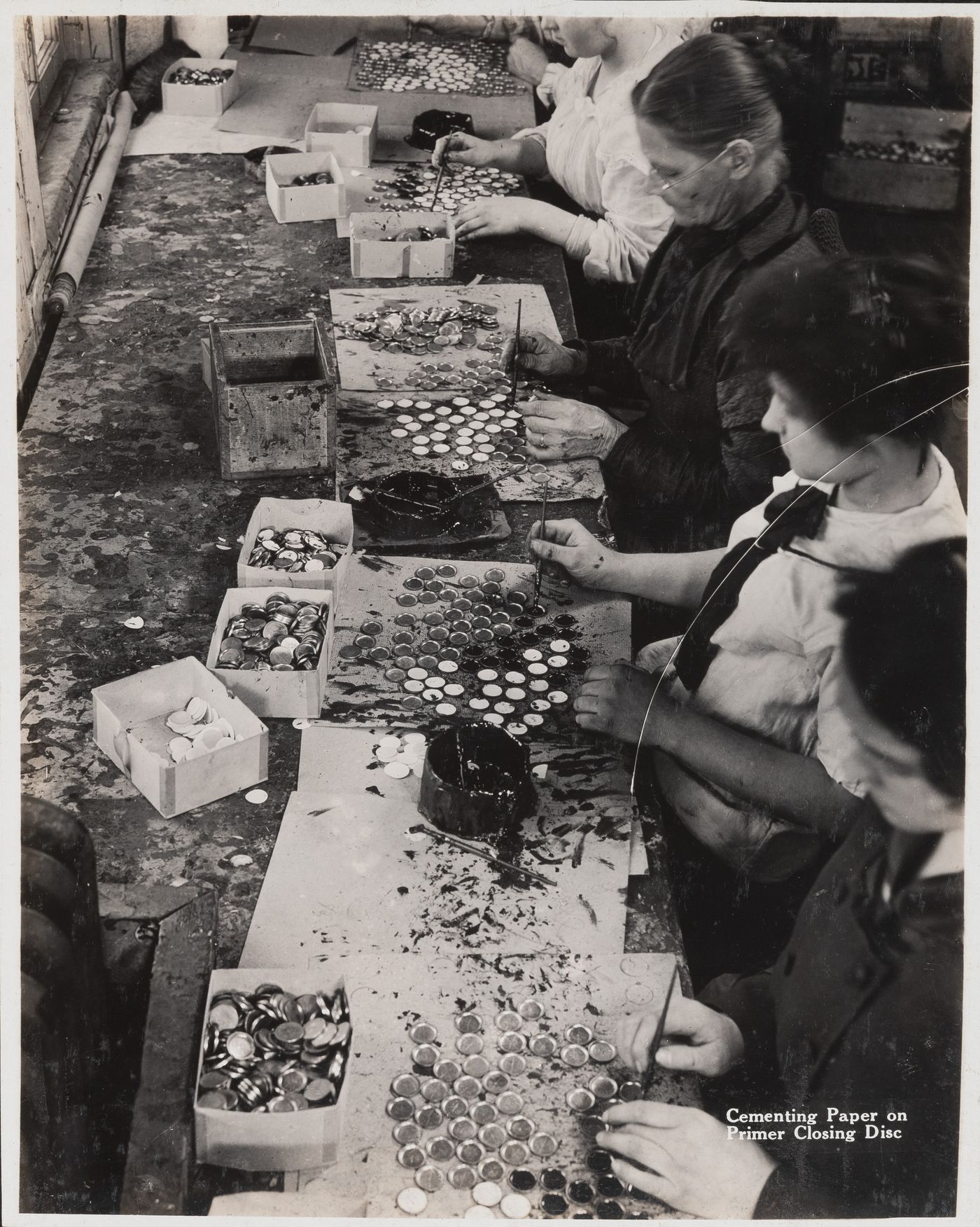 Interior view of workers cementing paper on primer closing disc at the Energite Explosives Plant No. 3, the Shell Loading Plant, Renfrew, Ontario, Canada