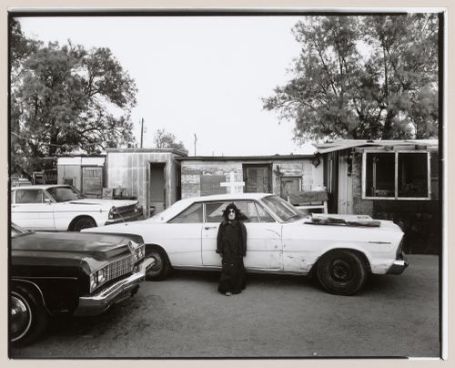 View of child wearing Halloween costume in front of car in yard with cross, Old Pascua, Tucson, Arizona, United States (from a series documenting the Yaqui community of Old Pascua)