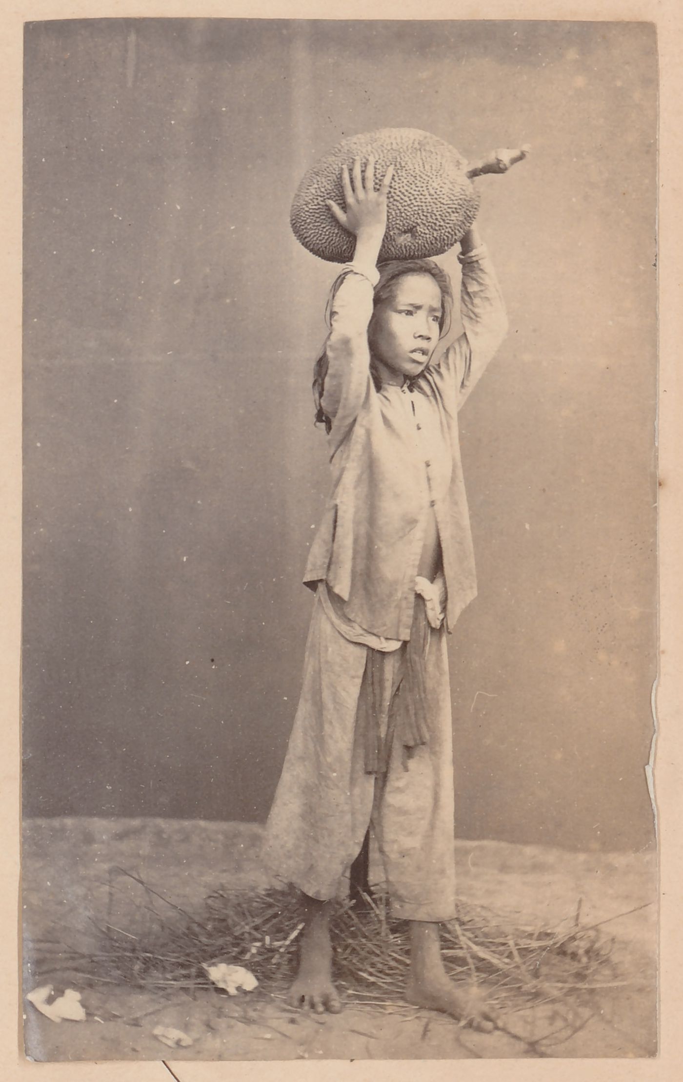 Portrait of a boy holding a durian fruit, probably in Cochin China (now in Vietnam)