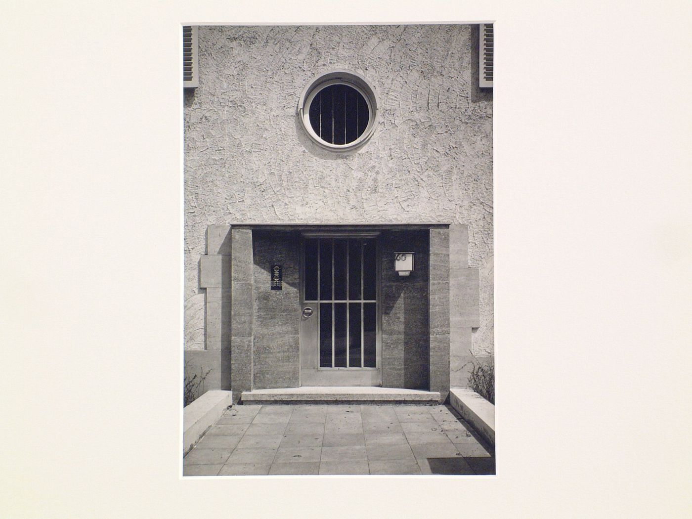 Detail, entrance to stucco house, with barred door, and round window above