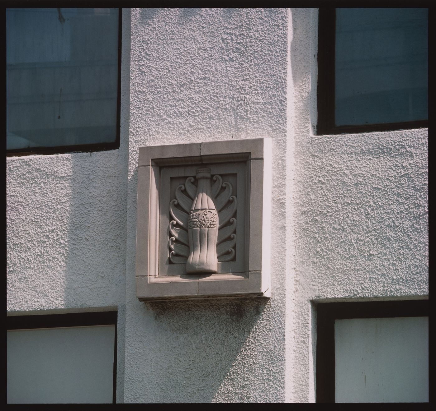 Detail view of sculptural relief of the Coca Cola bottle, on stucco wall of building