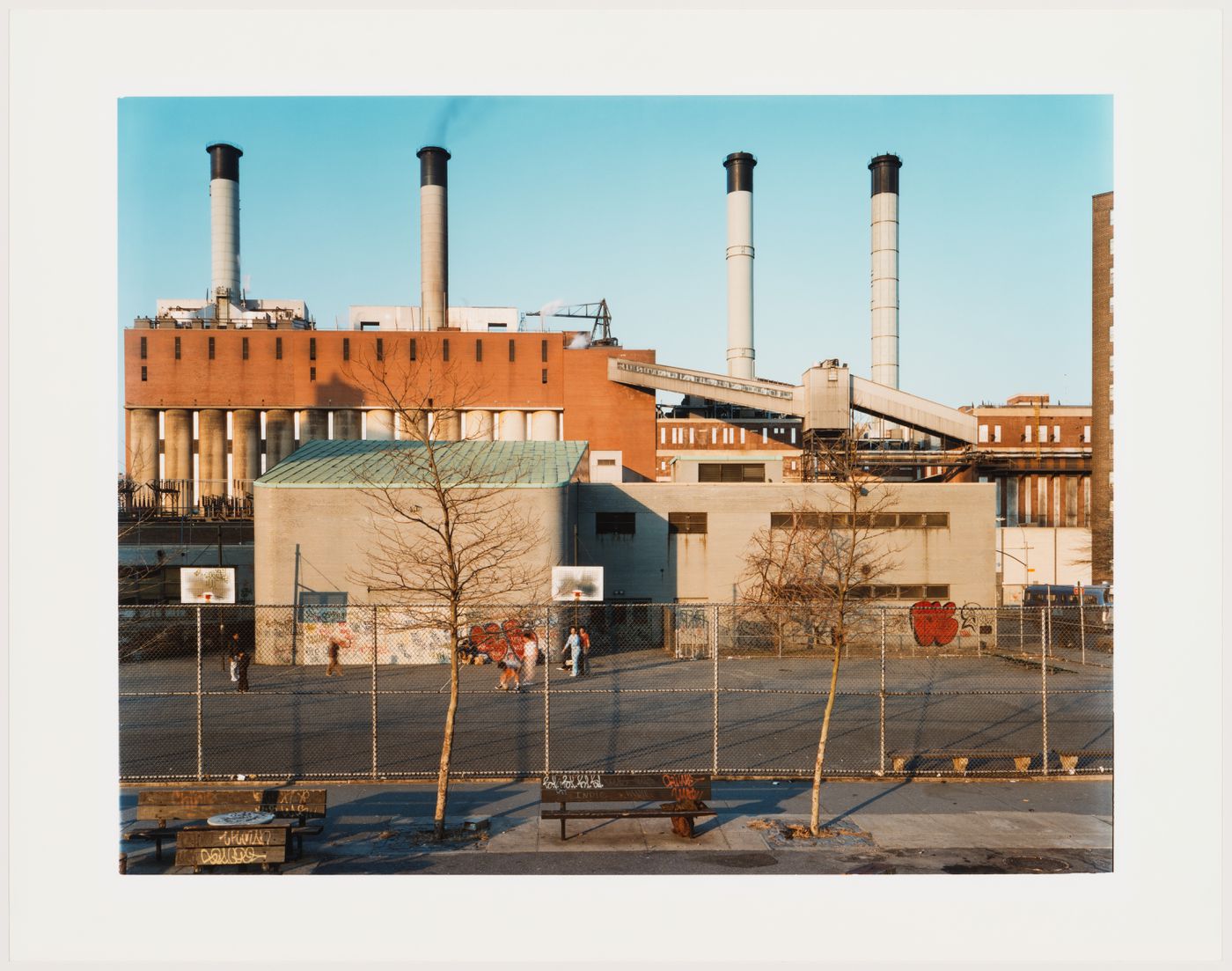 View from East 11th Street of people playing basketball in schoolyard with Con Edison power plant in background, New York City, New York, United States