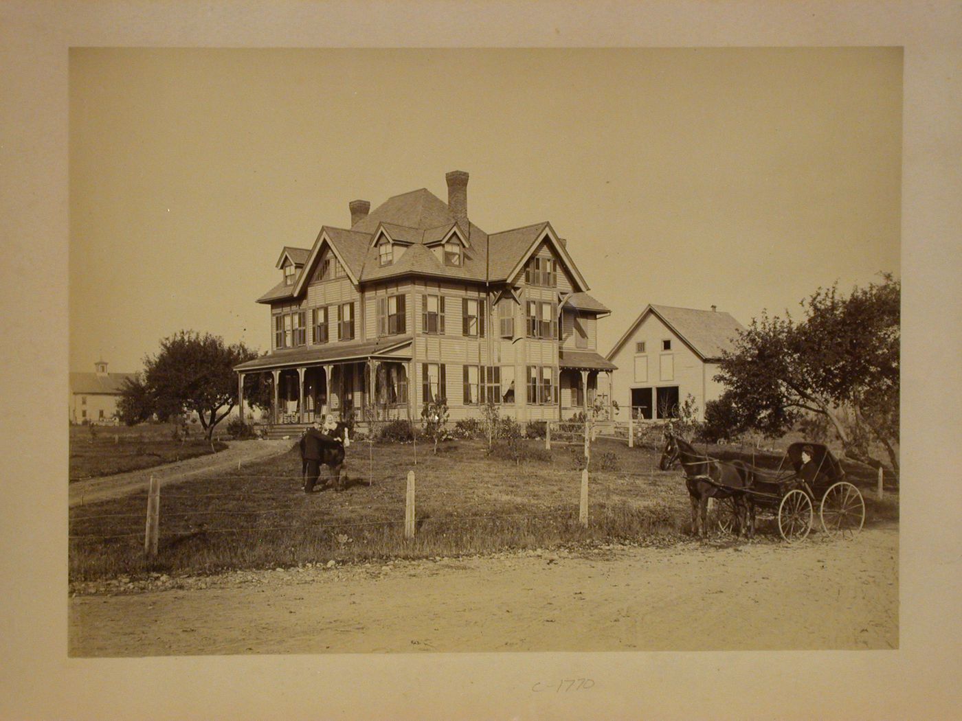 Large wood frame house, with man holding baby on horse in yard