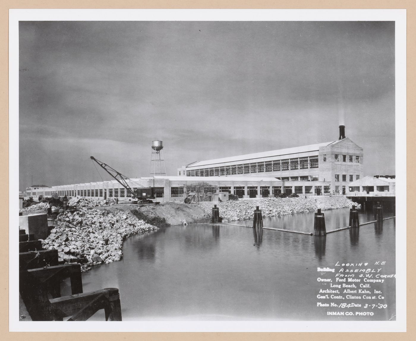 View of the south and east façades of the Assembly Building from the railroad bridge with a dock in the foreground under construction, Ford Motor Company Automobile Assembly Plant, Long Beach, California