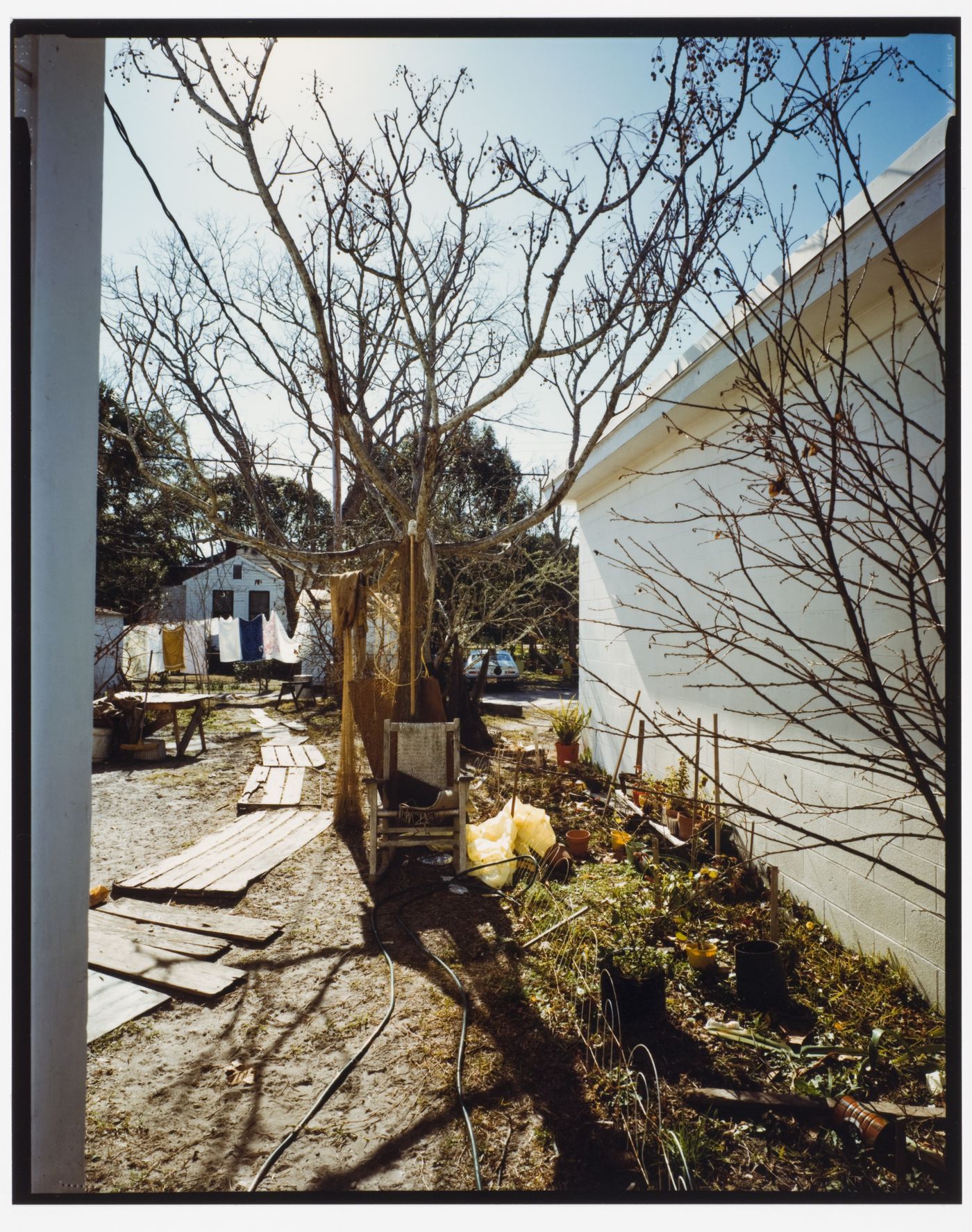 View of urban landscape with a tree with a chair in front of it next to the side of a building, off of U.S. 98, Apalachacola, Florida