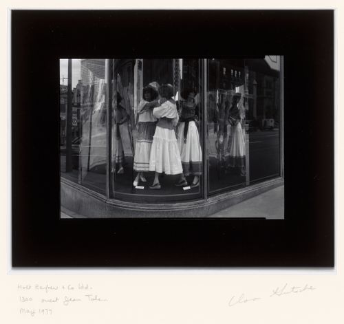 View of a display window of the Holt Renfrew store showing dresses and the reflection of buildings across the street, 1300-1312 rue Sherbrooke Ouest and 2200 rue de la Montagne, Montréal, Québec