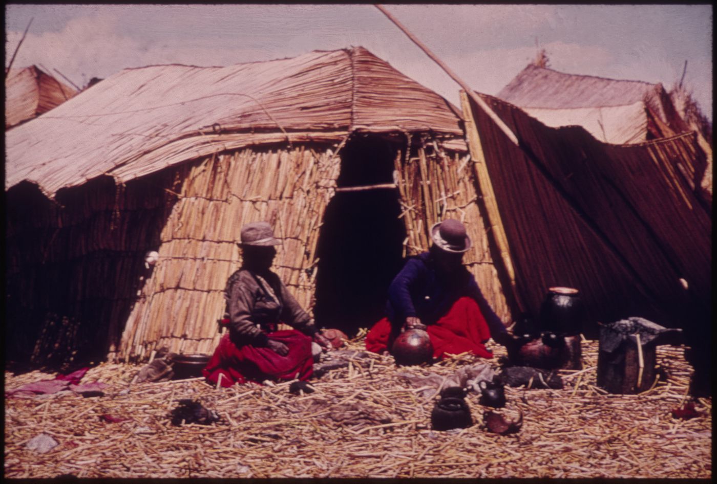 Two Qhas Qut suñi (Uru people) seated in front of a reed house, Lake Titicaca, Peru and Bolivia