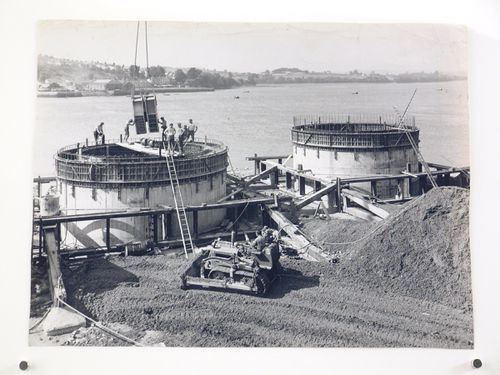 View of stairs being lowered by crane into round concrete structure by water, United Kingdom