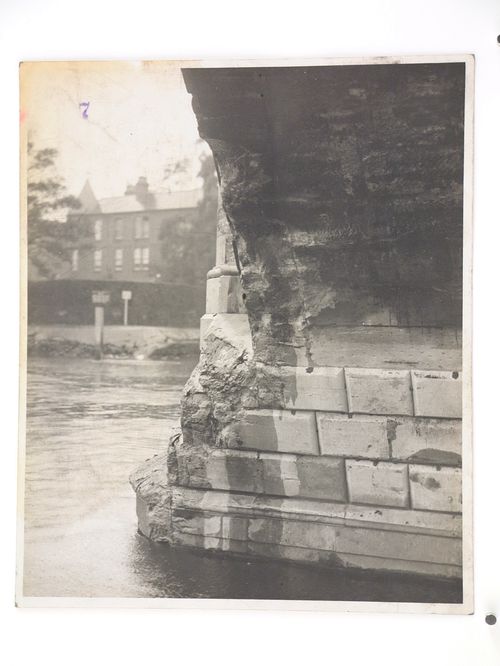 View of damage to the base of a stone arch bridge over water, United Kingdom