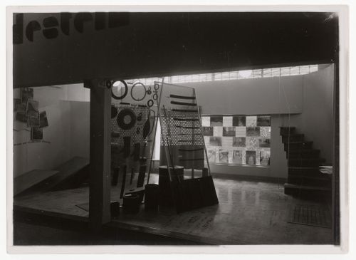 Interior installation view of an exhibition, showing photos mounted on window, and overlapped on wall, and freestanding sculptural elements, Netherlands