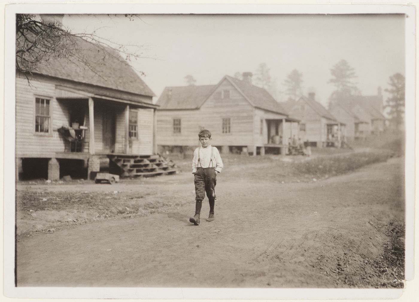 Photograph of Louis Stokes, one of the young workers in the Kosciusko Cotton Mills, walking along street with wooden houses, Kosciusko, Mississippi, United States
