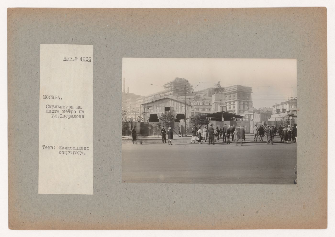 View of Sverdlova Square (now Teatral'naia Square) showing the subway station under construction surmounted by a sculpture of a worker and surrounded by hoardings, with the USSR Council of Ministers Building under construction in the background, Moscow